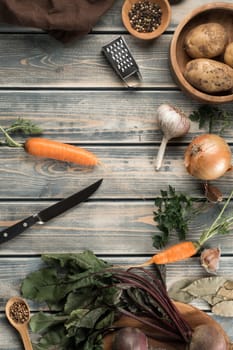 Knife for peeling carrots, flat lay. Kitchen tools for cooking. Mix of raw fresh organic vegetables on wooden table. Healthy food, ingredients. Zero waste, eco concept. Separate waste collection.