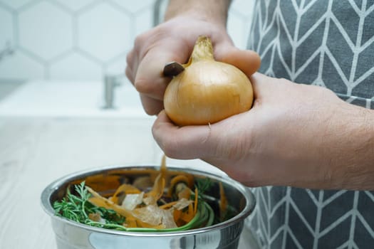 Male hands peeling by knife yellow onion over bowl of vegetable peelings closeup. Cook on kitchen table, prepare ingredients, food scrap. Healthy nutrition, vegetables. Separate waste collection.