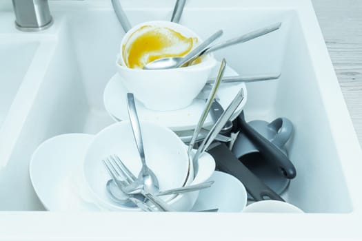 Sink full of pile of dirty tableware closeup. Dish washing, tableware after meal, food leftovers. Pile up sink with spoons, forks, knives, plates. Wash kitchen utensils manually. Home cleaning.