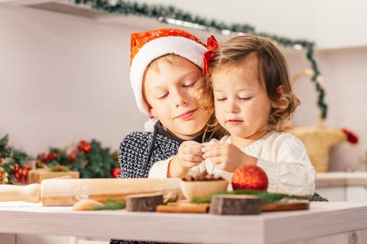 Cute little girl 2-4 with a red bow and boy 7-10 in a Christmas cap, making Christmas gingerbread cookies in the New Year's kitchen.