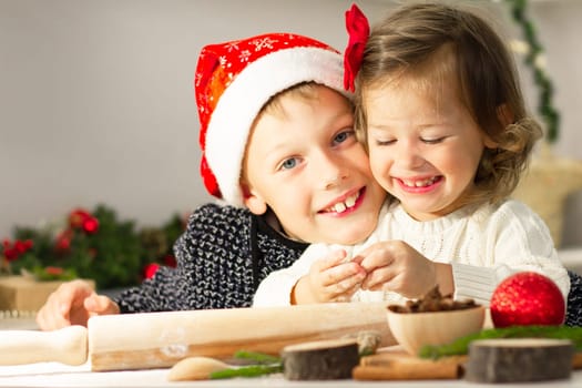 Cute little smiling girl 2-4 with a red bow and boy 7-10 in a Christmas cap, making Christmas gingerbread cookies in the New Year's kitchen.