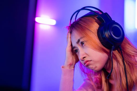 Game Over. Asian gamer playing online video game she losing and sad on computer PC colorful neon LED lights, young woman in gaming headphones feeling disappointed about lost game, E-Sport concept