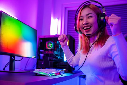 Winning. Happy Gamer young plays online video games computer she raises hands to wins tournament, young woman in gaming headphones playing video game online at home feel excited, E-Sport concept