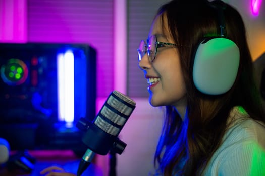 Asian young gamer woman wear headphones playing video games online on computer she live stream and chat with fans, Happy streamer female talking with microphone in gaming room, game streaming concept