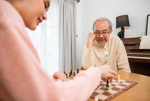 Smiling senior elderly having fun playing chess game with beautiful daughter at home, nurse caregiver in nursing home for leisure, Happy active retired people, Healthcare and medical homecare concept
