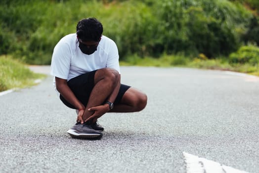 Close up Asian young sport runner black man wear watch hands joint hold leg pain because of twisted ankle broken while running at the outdoor street health park, healthy exercise Injury from workout