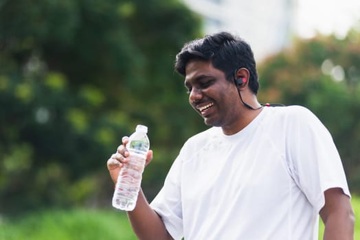 Close up Asian young sport runner black man wear athlete headphones he drinking water from a bottle after running at the outdoor street health park, healthy exercise workout concept