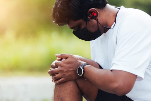 Close up Asian young sport runner black man wear watch sitting hands joint hold knee pain during the run while running at the outdoor street health park, healthy exercise injury from workout concept