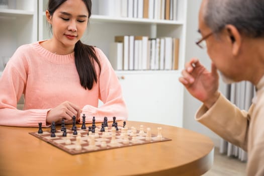 Beautiful young smile woman having fun sitting playing chess game with senior elderly at home, nurse caregiver in nursing home for leisure, Happy active retired people, Healthcare and medical concept