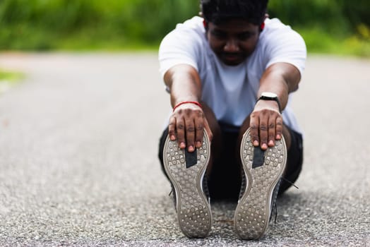 Close up Asian young athlete sport runner black man wear watch he sitting pull toe feet stretching legs and knee before running at outdoor street health park, healthy exercise before workout concept