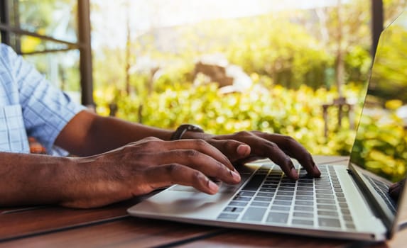 Happy Asian black businessman person or office worker wear face mask protect sitting on desk work from home using laptop computer typing keyboard and connect networking online at the coffee cafe shop