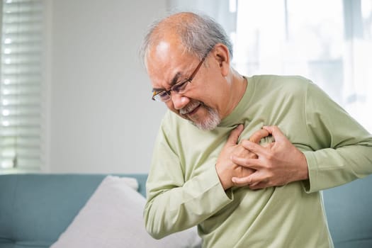 Asian older man have congenital disease suffering from heartache alone at home, Senior man bad pain hand touching chest having heart attack, Old age retirement health problems unhealthy diseased