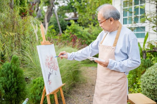 Lifestyle artist. Senior old man painting picture artwork using brush and water color on canvas, portrait elderly white haired paint at his easel outside green nature, Happy retirement and activity