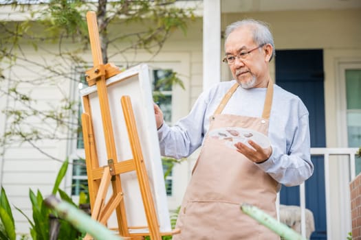 Lifestyle elderly people smile paint at his easel outside home, Asian senior old man painting picture using brush and oil color on canvas, Happy retirement artist and activity concept