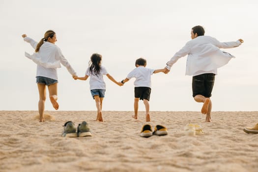 Happy family day. Back view of Asian having family parents with child fun holding hands together running to beach, lifestyle father, mother and kids relax take off shoes run on sand, holiday travel