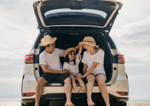 Happy Family Day. Dad, mom and daughter enjoying road trip sitting on back car, Parents and children traveling in holiday at sea beach, family having fun in summer vacation on beach with automobile