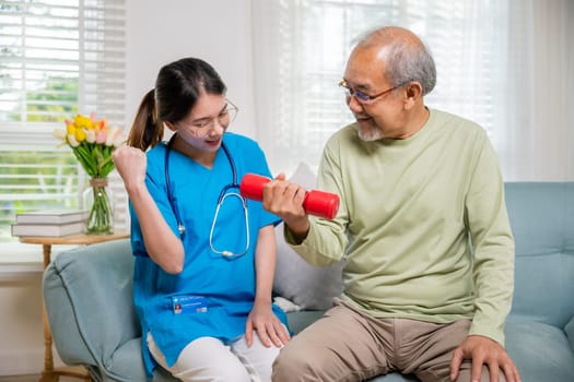 Young nurse physiotherapist helping old man in lifting dumbell at home, Asia nurse support elderly retirement sitting on sofa using red dumbbell workout exercise physical recovery, Health care concept