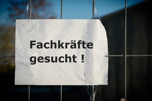 Notice on the fence of a company in Germany with the inscription Fachkrafte gesucht. Translation of the text: Professionals wanted