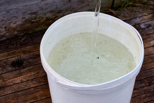 a white plastic bucket is filled with water from the pump. High quality photo