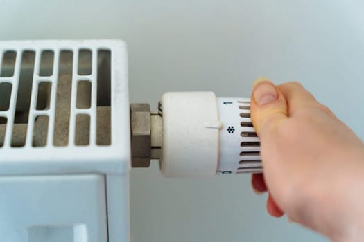 female hand completely turns off the heating radiator in apartment due to the rising cost of heating and utilities because of the energy crisis.