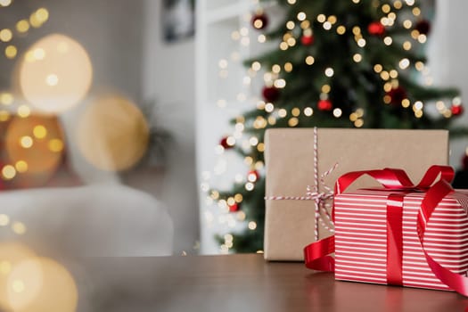 Christmas, New Year background with copy space. Empty wooden tabletop surface, defocused decorated Christmas fir tree composition, bokeh sparkle lights effect, red gift boxes. Product montage mockup