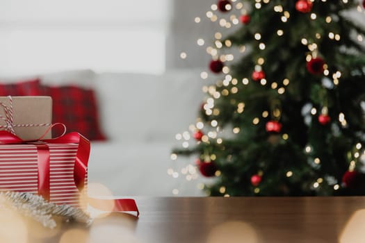 Christmas, New Year background with copy space for design. Empty wooden tabletop surface, blurred defocused decorated Christmas fir tree composition, bokeh sparkle lights effect, red boxes with gifts