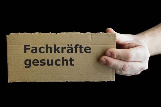 one hand holds a sign with german inscription Fachkrafte gesucht, with black background. Translation: Skilled workers wanted