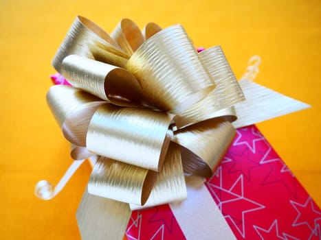 Red pink gift box with a large golden bow on a yellow ocher color background. Gift for Christmas, New Year, Birthday, Mother's Day, Wedding, Valentine's Day. Beautiful festive decoration. Give gifts