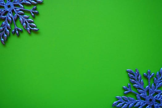 Christmas background with snowflakes. On a green background, two silver-blue snowflakes with sparkles are laid out. Happy New Year. Merry Christmas. Postcard or invitation. Copy space. Flat lay