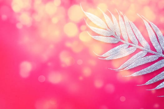 Artificial festive exotic silver branch with long leaves on a bright pink or red background. Copy space. Flat lay. Free space for text. New Year, Christmas, birthday background. Yellow bokeh.