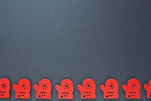 New Year and Christmas decorations in the form of red cardboard mittens with sparkles. The mittens are lined up along the bottom edge of the black paper. Christmas background. Copy space.