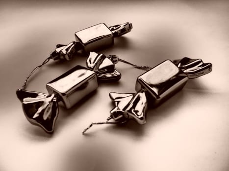 Christmas decorations in the form of sweets. Three candies in wrappers. Beautiful unusual decorations for New Year and Christmas. Hanging threads. Sepia brown beige monochrome toning