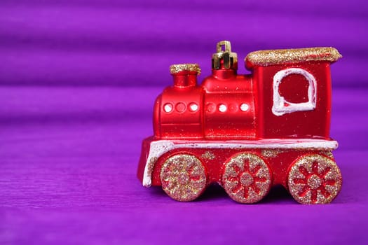Red toy train locomotive on a purple and lilac gradient background. New Year or Christmas card. Icicles and snow on a train. Free space for text. Copy space. Festive background