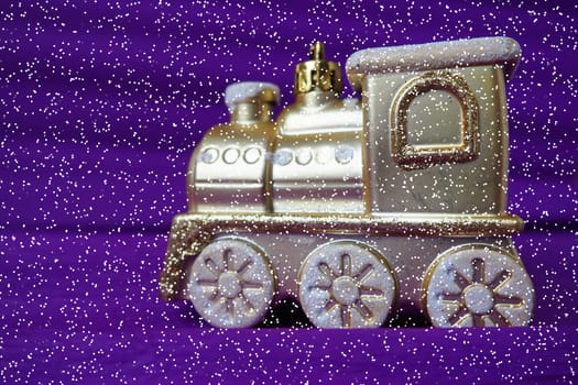 Golden toy train locomotive on a purple and lilac gradient background. New Year or Christmas card. Icicles and snow on the train. Free space for text. Copy space. Festive falling snowflakes bokeh