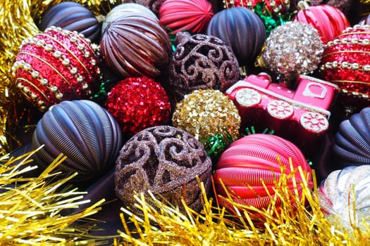 Christmas background with yellow tinsel and Christmas balls. Beautiful Christmas toys and decorations. Red, gold, brown, silver, yellow striped shiny balls. Toy festive train locomotive