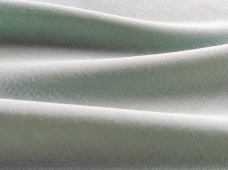 Beautifully folded light green fabric. Soft pleasant waves and flounces on textiles. Close-up. Drapery for curtains, fabric for dressmaking or upholstery.