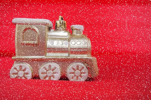 Golden toy train locomotive on a red and pink gradient background. New Year or Christmas card. Icicles and snow on a train. Free space for text. Copy space. Falling snowflakes