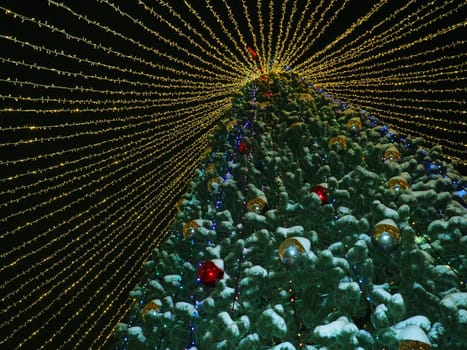 big beautiful Christmas Tree with decorations and Illuminations in snowy night. New Year and Christmas holiday background. Festive winter city landscape