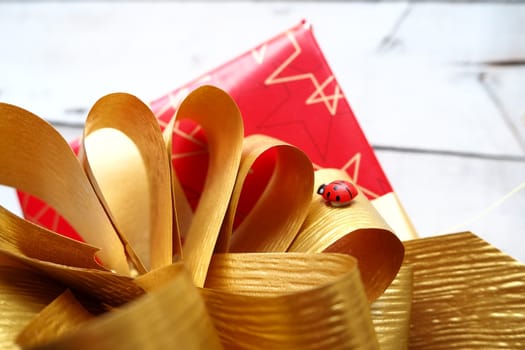 Red gift box with a large gold bow on a wooden background painted with white paint. Gift for Christmas, New Year, Birthday, Mother's Day, Wedding, Valentine's Day. Beautiful festive decoration.
