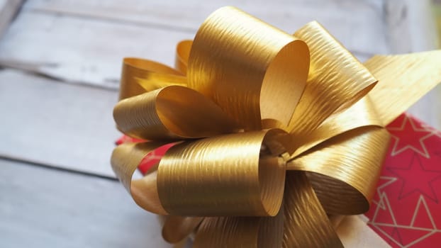 Red gift box with a large gold bow on a wooden background painted with white paint. Gift for Christmas, New Year, Birthday, Mother's Day, Wedding, Valentine's Day. Beautiful festive decoration.