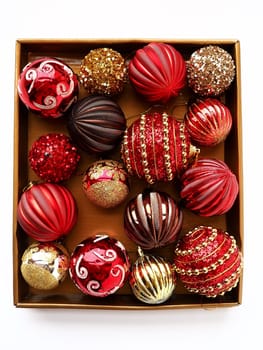 Christmas decorations in a box on a white background. Beautiful red and gold balls with sparkles and stripes. Preparing for the New Year Christmas holidays. Beautiful decorations. Copy space isolated