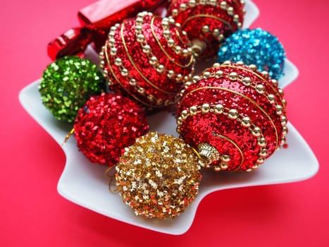 Multicolored Christmas balls and candies on a white plate in the shape of a Christmas tree. Red pink background. Beautiful striped red, pink, green, silver, yellow, blue, gold Christmas decorations