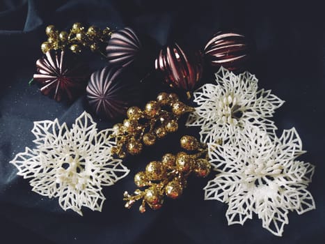 card for the new year and christmas with decorations, Christmas decorations and sparkles on a black background. Brown shiny striped balls, flowers and white snowflakes, golden twigs with berries.
