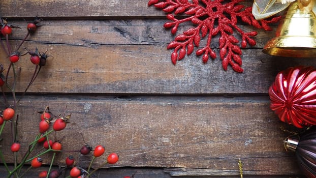 New Year's or Christmas still life. Golden bell. Red fruits of wild rose or rose bush on a wooden background. Red and brown striped Christmas balls. Red carved star with sparkles.