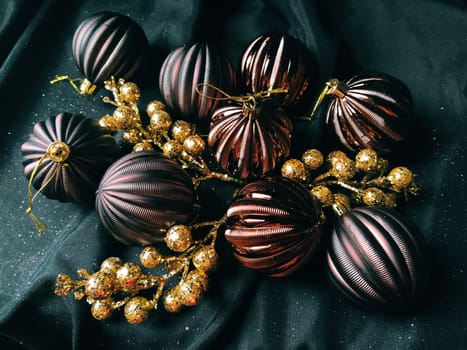 card for the new year and christmas with decorations, Christmas decorations and sparkles on a black background. Brown shiny striped balls, flowers and white snowflakes, golden twigs with berries.