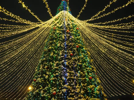 big beautiful Christmas Tree with decorations and Illuminations in snowy night. New Year and Christmas holiday background. Festive winter city landscape