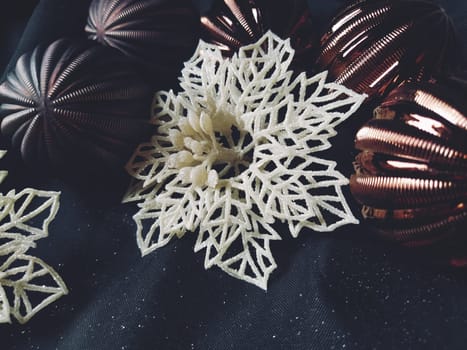 card for the new year and christmas with decorations, Christmas decorations and sparkles on a black background. Brown shiny striped balls, flowers and white snowflakes, golden twigs with berries.