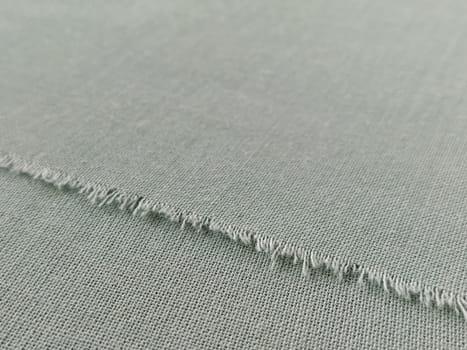 Ripped edge of fine woolen fabric in green or blue. Loose threads at the edge of a piece of textile. Close-up. Woven background. Calm green pastel color.