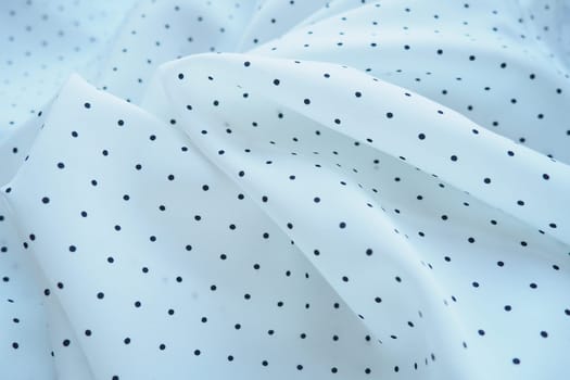 Texture of silk fabric. Black polka dots on a white background. Dress lightweight synthetic fabric in white with a repeating pattern. The textile is made up of waves and folds. Feminine classic style