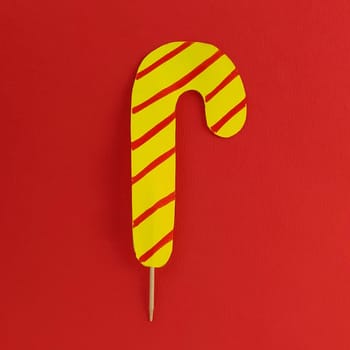 Lollipop on a red background. Imitation of yellow candy with red stripes. New Year or Christmas decoration. Copy space. Lollipop in the middle of the image.